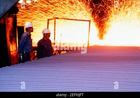 Side profile of two foundry workers standing in a steel plant