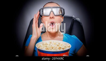 A young woman in the cinema is watching a movie in 3D glasses and with popcorn in her hands. Stock Photo