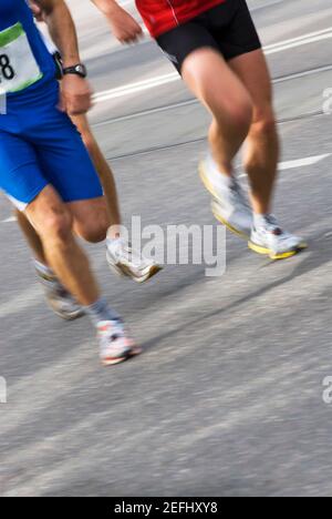 Low section view of three male athletes running on a running track Stock Photo