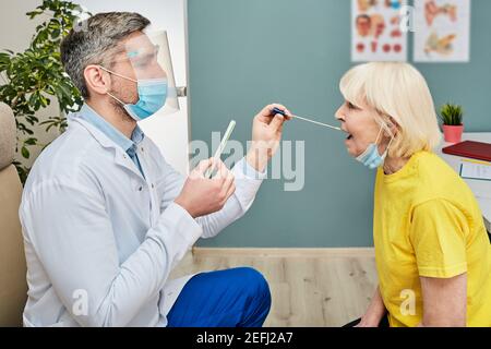 Male doctor taking an elderly female oral swab for coronavirus specimen collection. PCR test of COVID-19 for senior people Stock Photo