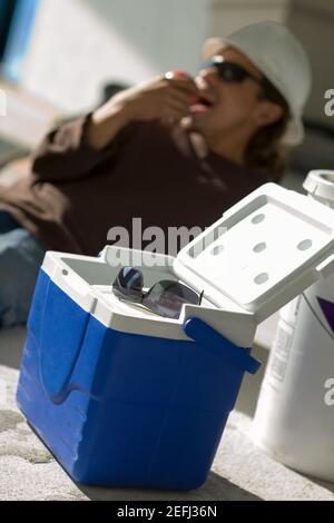 Close-up of a cool box with a young man eating an apple in the background Stock Photo