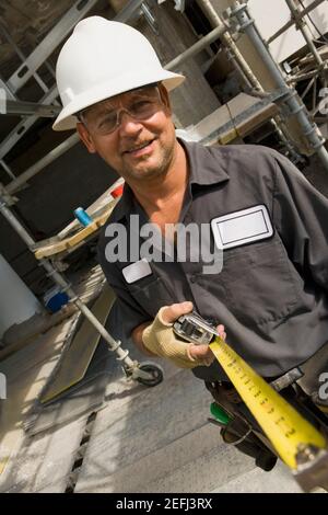 Portrait of a male construction worker holding a tape measure and smiling Stock Photo