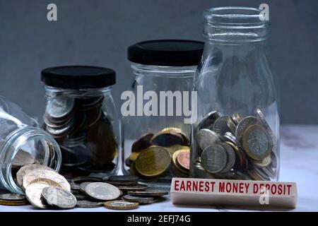 Text on wood block and glass jars with multicurrency coins - Earnest money deposit Stock Photo