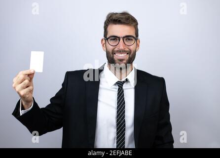 Young business man wearing suit smiling and holding white card Stock Photo