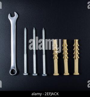 Spanner and long dowels with metal self tapping screw, on black background. Stock Photo