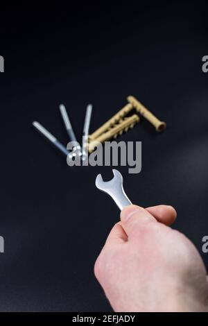 Hand holding wrench close up and long dowels blured on black background. Stock Photo