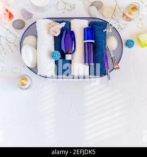 Cosmetic Spa background. Place your design. Blue cosmetic bottles on folded towels in a basket with seashells on a white background with copy space. B Stock Photo