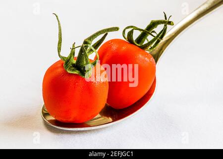 Close-up of two red tomatoes on a spoon on a white tablecloth, London, UK Stock Photo