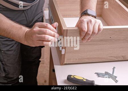 Caucasian mans hands assembling furniture using a screwdriver. Moving in, housework. Close-up. Stock Photo