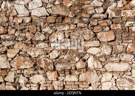 Old stone wall, painted in a faded white color and built with stones and mud Stock Photo