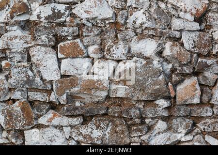 Old stone wall, painted in a faded white color and built with stones and mud Stock Photo