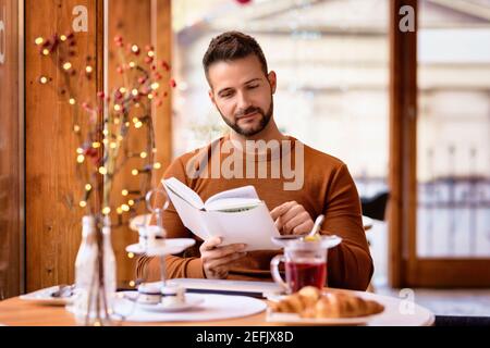 Candid shot of smiling man sitting in the cafe and reading book. Stock Photo