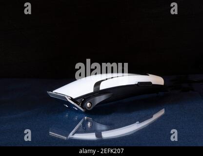 An electric razor for cutting hair is lying on a glass table. Equipment and tools on a black background Stock Photo