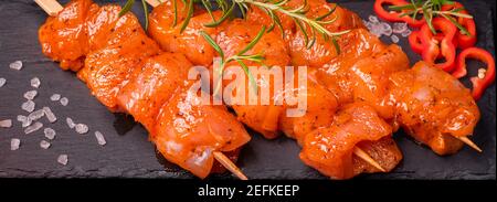 Chicken pieces of kebabs marinated in a red marinade with spices on a dark culinary board,on a background with pieces of pepper. Raw chicken pieces on Stock Photo
