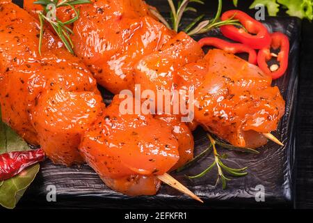Chicken pieces of kebabs marinated in a red marinade with spices on a dark culinary board,on a background with pieces of pepper. Raw chicken pieces on Stock Photo