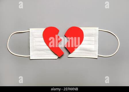 Protective surgical mask split in two with a broken heart on a gray background.Concept of divorce due to the 2019 coronavirus pandemic Stock Photo