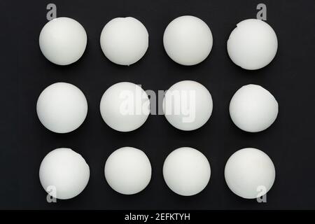 White eggshells are laid out in even rows on a black background. The concept of sameness, equality and equity. The concept of impersonal, stereotyped Stock Photo