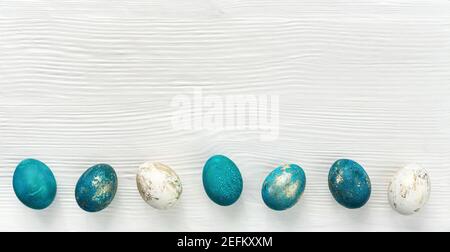 Horizontal Easter banner with colorful eggs painted in turquoise, blue and gold. Easter eggs on white wooden background for loft minimal  style poster Stock Photo