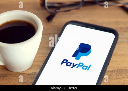 Galicia, Spain; february 15, 2021: Paypal logo on Smart phone screen on desk with eyeglasses and cup of coffee on wooden table Stock Photo