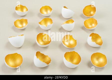 Eggshell, painted from the inside in gold color, lies in even rows on a beige background. Harmonious combination of gold, white and ecru colors. Conce Stock Photo
