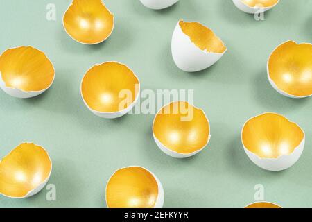 An example of gold and smoky green colors combination. Eggshell painted inside with gold paint isolated on green. Modern concept of festive Easter adv Stock Photo