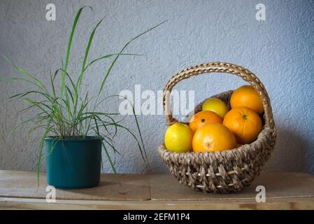 A woven basket full of citrus fruits besides a pot of lemongrass Stock Photo