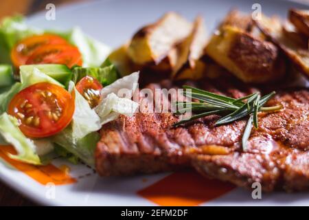 Grilled pork with baked potatoes and with salad. The food is served on a plate. Delicious grilled meat. Roasted pork steak on the white plate. Stock Photo