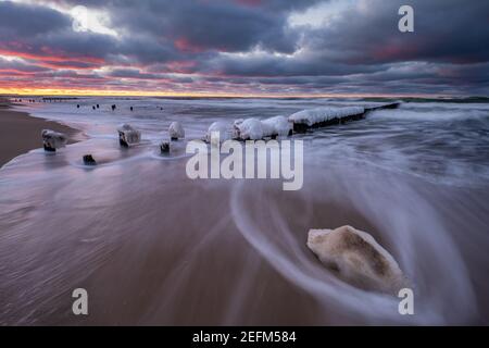 Beautiful winter sea landscape. Ice breakwaters, waves and fiery sunset. Artistic photography. Stock Photo