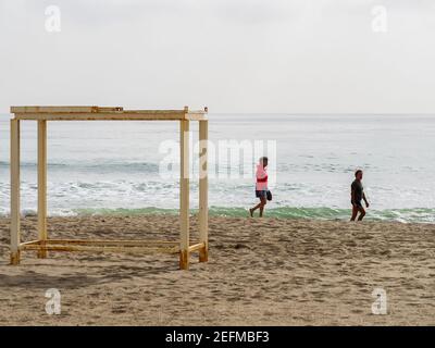 Fuengirola, Malaga, Spain. 02/05/2021.    Older couple walking together behind a beach bed structure on the sand of the beach in Fuengirola on a sunny Stock Photo