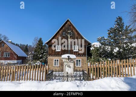 Wooden cottage in the village. Typical mountain hut in winter on a sunny day. Wooden cross in front of the cottage. Stock Photo