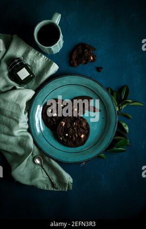chocolate cookies with black cup of tea on the turquoise plate  with spoon on the blue background. flat lay Stock Photo