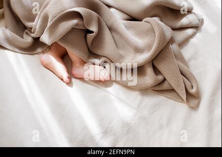 Baby little feet covered with lightweight cotton baby knit blanket Stock Photo