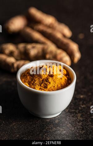 Indian turmeric powder and root. Turmeric spice. Ground turmeric in bowl on black table. Stock Photo