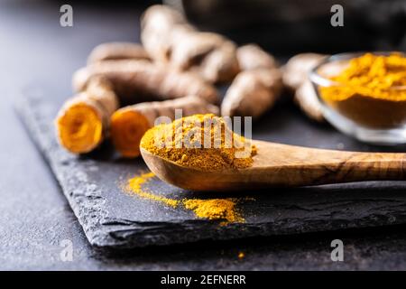 Indian turmeric powder and root. Turmeric spice. Ground turmeric in wooden spoon. Stock Photo