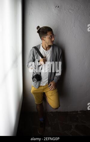 Young stylish photographer holds his camera and leans on a white wall. Photographer concept Stock Photo