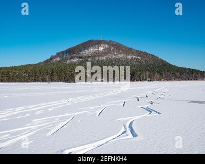 Fresh powder snow on the frozen Machovo Lake with traces of ice skaters. In the background the frosty Borny hill with the transmitter tower. Stock Photo