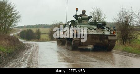 British Army Warrior FV 512 MRV tank towing a Warrior FV 510 with a broken missing track in pouring rain Stock Photo