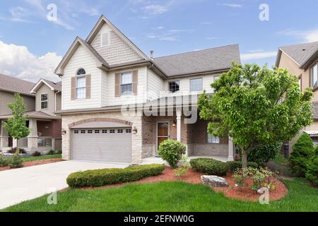 A new suburban house with half light brown siding and have brick and stone, brown window shutters, and a front porch. Stock Photo