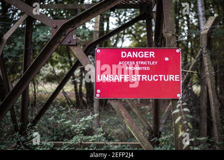 Danger Unsafe Structure sign attached to rusty old metal tower which is in a run down derelict condition keep out risk of injury Stock Photo