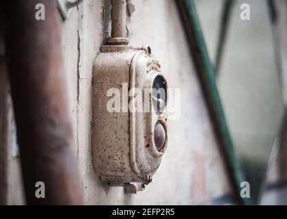 Art Deco 1950s retro old iron electrical light power switch with red press button to start and stop in abandoned old hospital rusty and worn out Stock Photo