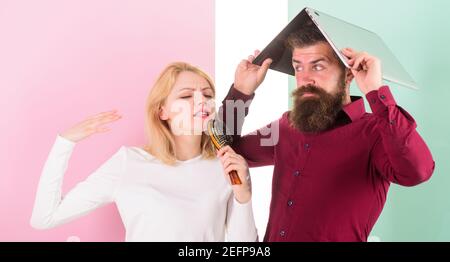 Crazy about her voice. Lady imagine she superstar talented singer. Lady awful voice sing using hair brush as microphone while man annoyed hiding under laptop. Man fed up listening her creepy voice. Stock Photo