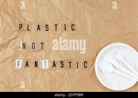 Disposable appliances plate, fork, spoon, knife, phrase from letters on transparent base Plastic not fantastic on brown crumpled craft paper. Eco, zer Stock Photo