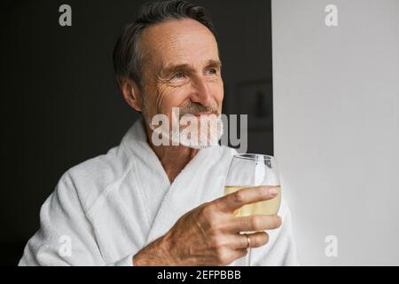 Close up of smiling mature man wearing white bathrobe holding wineglass Stock Photo
