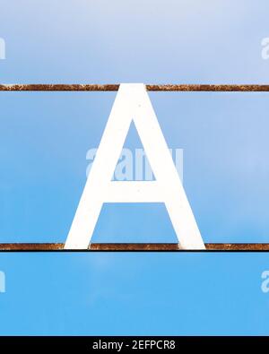 White letter A attached to rusty metal bars against a blue sky Stock Photo