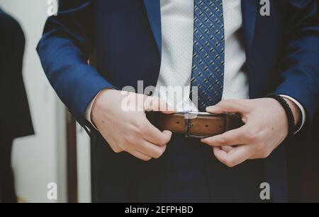 Closeup of an elegant man in a blue suit adjusting the leather belt on h Stock Photo