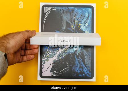 Paris, France - Nov 16, 2018: POV point of view personal perspective male hand holding the new AApple Pencil cardboard package with iPad Pro package isolated on a yellow background - unboxing process Stock Photo