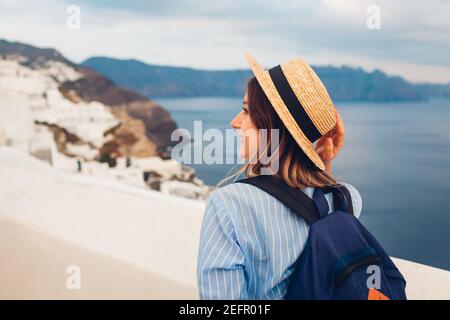 Tourist woman walking on Santorini island, Greece enjoying sea and city landscape. Traveler with backpack admires Caldera view in Oia Stock Photo