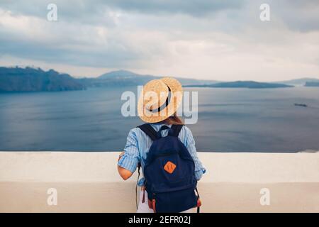 Tourist woman walking on Santorini island, Greece enjoying sea landscape. Traveler with backpack enjoys Caldera view in Oia Stock Photo