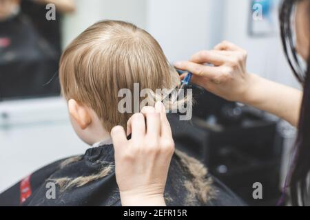 Hairdresser barbershop cuts the hair of blonde child boy with scissors. Haircut hairstyle close-up. Stock Photo