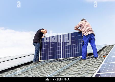 solar panels. Electrical engineers mans are working installing solar panels on solar station on house roof against blue sky. Development sun alternati Stock Photo